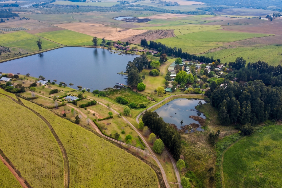 An expansive aerial view of a rural residential estate featuring a large lake, smaller pond, surrounding farmland, and established woodland areas.