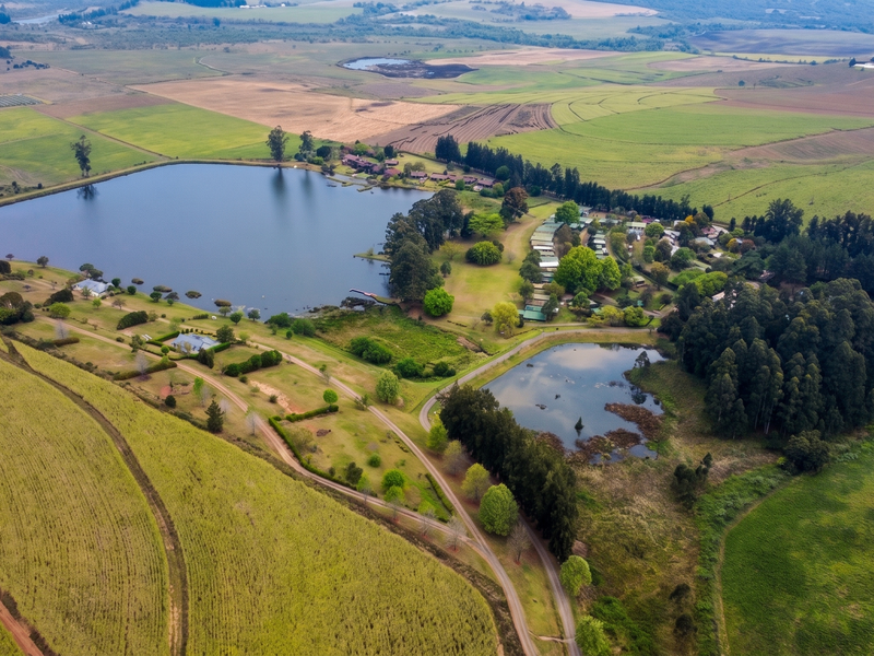 An expansive aerial view of a rural residential estate featuring a large lake, smaller pond, surrounding farmland, and established woodland areas.