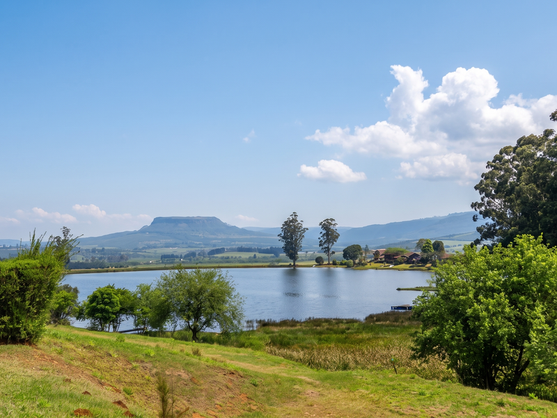 A scenic view of a tranquil lake surrounded by lush greenery, mature trees, and distant mountain ranges, showcasing the natural beauty of the property.