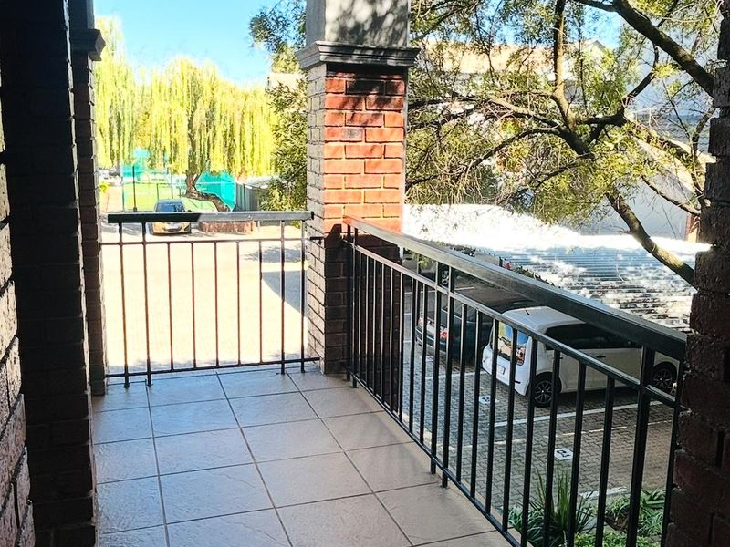A covered balcony featuring tiled flooring, brick support pillars, and a metal balustrade overlooking the parking area.