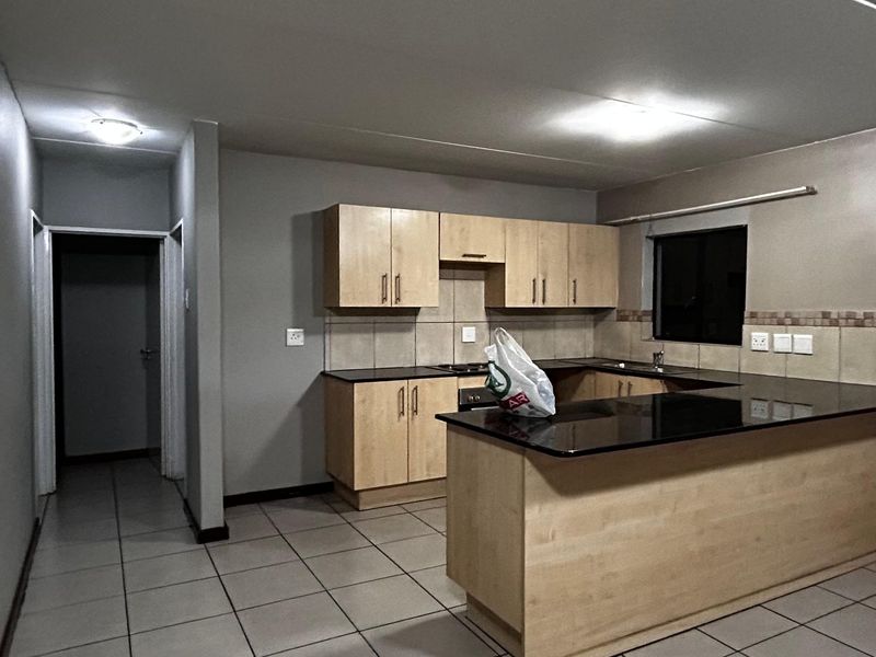 A functional kitchen featuring light wood cabinetry, black granite countertops, tiled flooring, and a breakfast bar island.