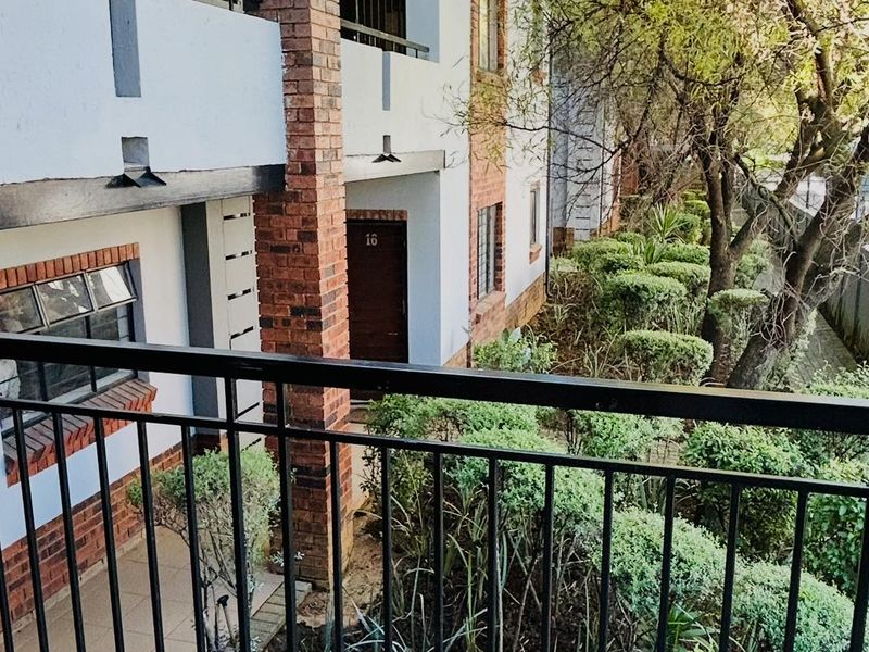 A tiled balcony with a metal balustrade overlooking the apartment complex garden and exterior brick facade.