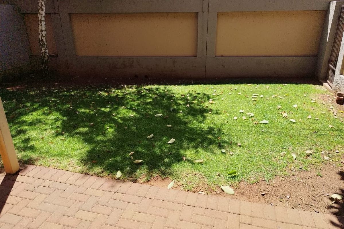 A private rear garden area featuring a paved patio and a grass lawn enclosed by a solid perimeter wall.