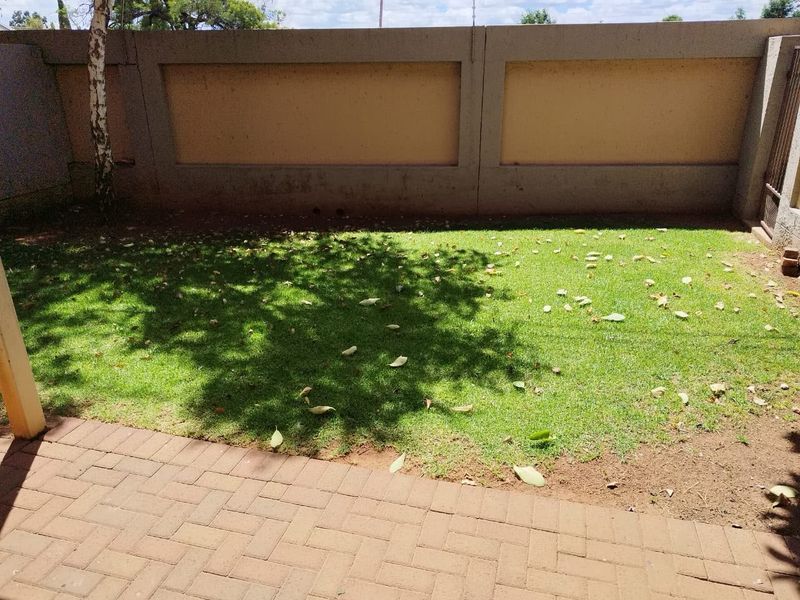 A private rear garden area featuring a paved patio and a grass lawn enclosed by a solid perimeter wall.