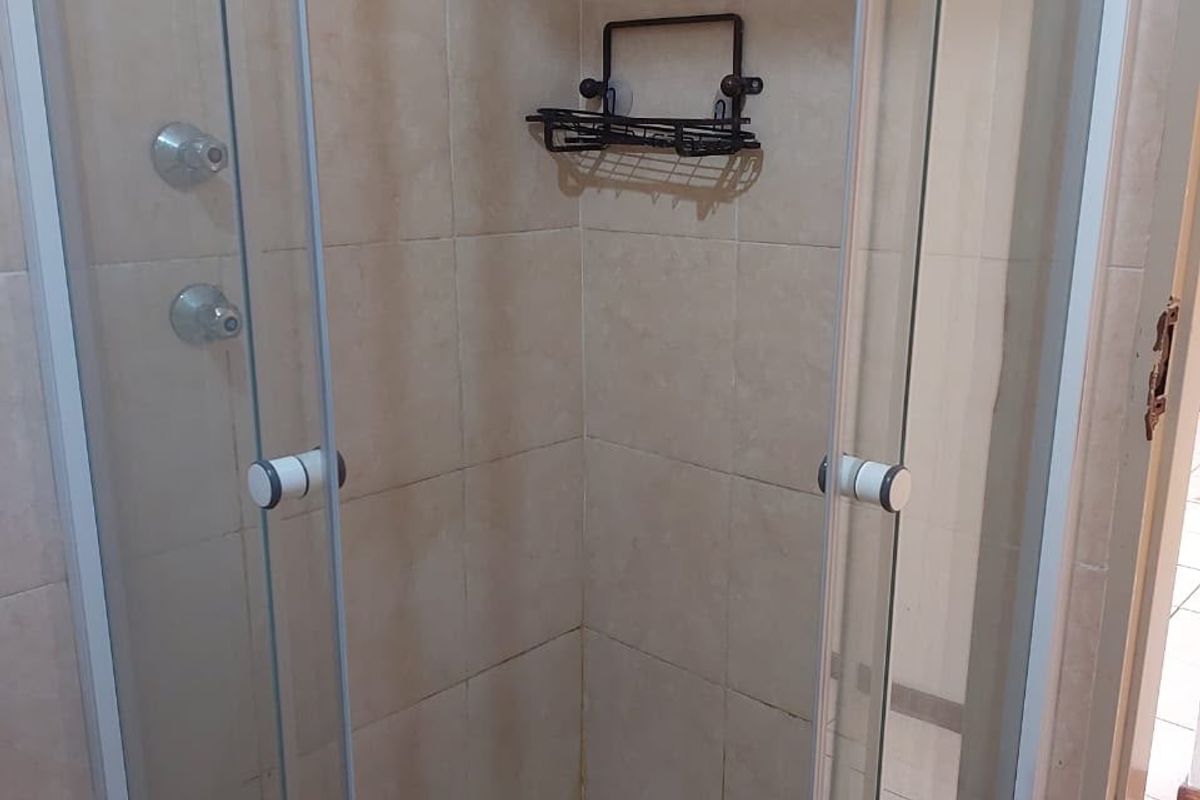 A compact corner shower unit featuring a glass enclosure, tiled walls, and standard shower fixtures.