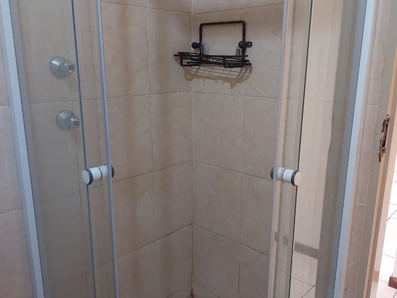 A compact corner shower unit featuring a glass enclosure, tiled walls, and standard shower fixtures.