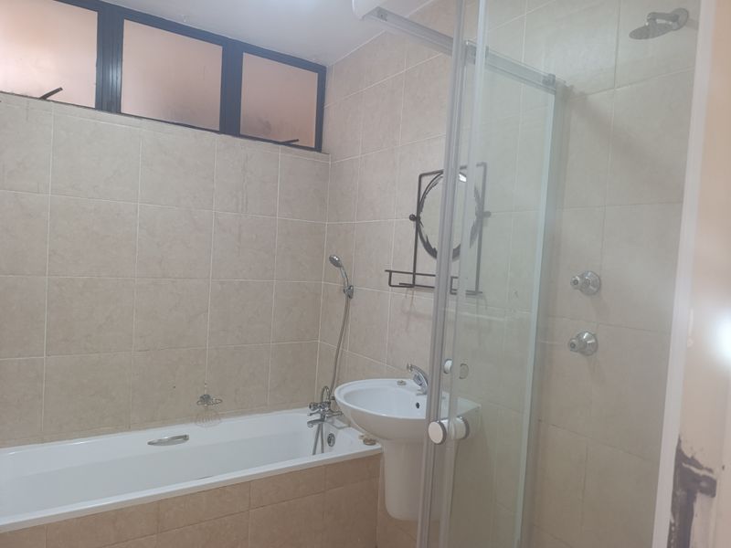 A functional bathroom featuring a bathtub, pedestal sink, and a separate glass-enclosed shower area with neutral wall tiling.