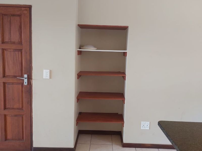 An open plan living area featuring tiled flooring, a solid wooden door, and built-in wall shelving, providing a neutral base for interior design.