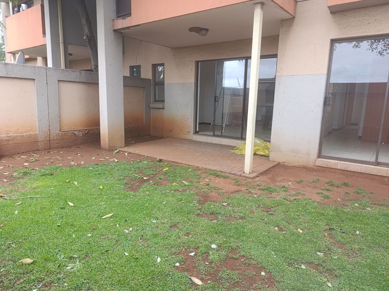 Rear exterior view of an apartment featuring a paved patio area, sliding glass doors, and a private garden space with boundary walling.