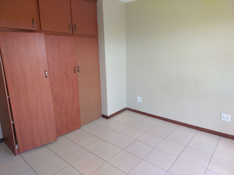 An empty bedroom featuring tiled flooring and built-in wooden cupboards, providing a neutral canvas for personalization.