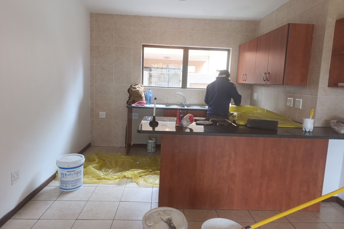 A functional kitchen featuring built-in wooden cabinetry, granite countertops, a stainless steel sink, and tiled finishes, currently undergoing maintenance.