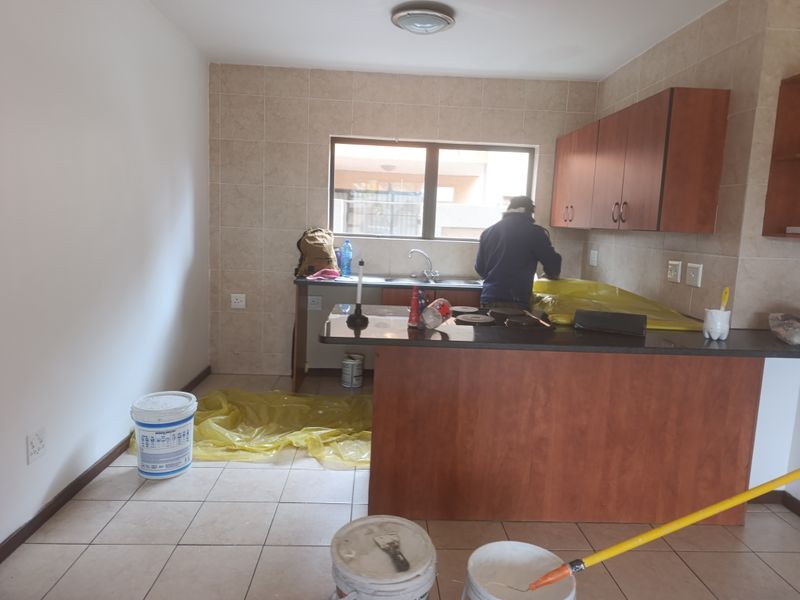 A functional kitchen featuring built-in wooden cabinetry, granite countertops, a stainless steel sink, and tiled finishes, currently undergoing maintenance.