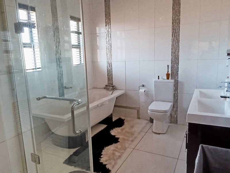 Modern bathroom featuring a double vanity, glass-enclosed shower, and a freestanding bathtub with elegant mosaic tile wall accents.