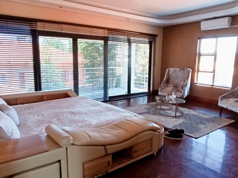 Spacious bedroom featuring timber flooring, recessed ceiling lighting, a split-system air conditioner, and large sliding glass doors with venetian blinds.