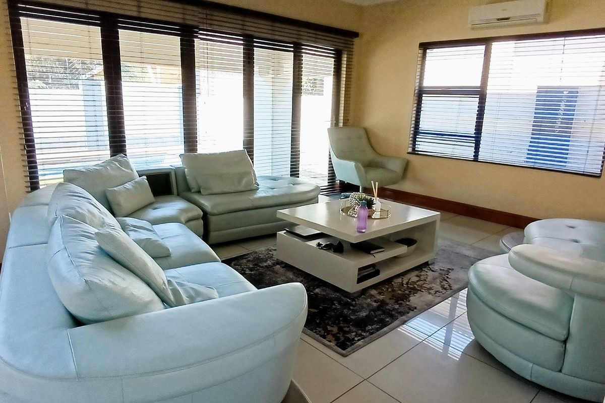 A bright living room featuring large windows with venetian blinds, tiled flooring, and a wall-mounted air conditioning unit.