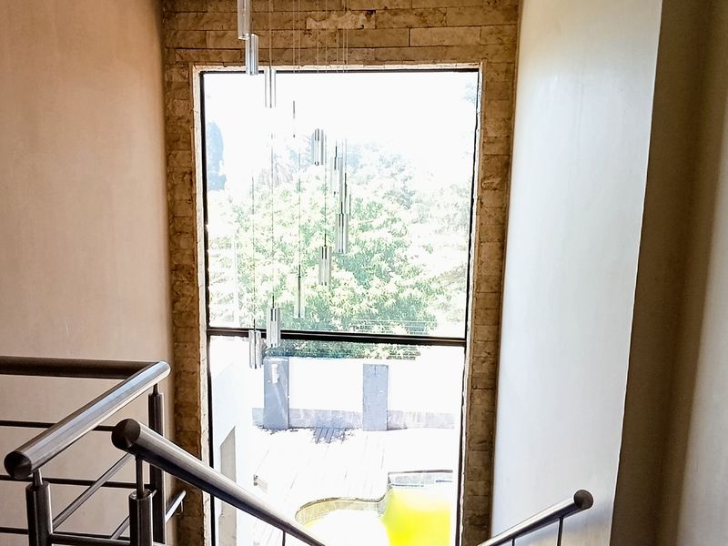 A bright hallway featuring a modern stainless steel balustrade, a stone-clad feature wall, and a large window overlooking the outdoor pool area.