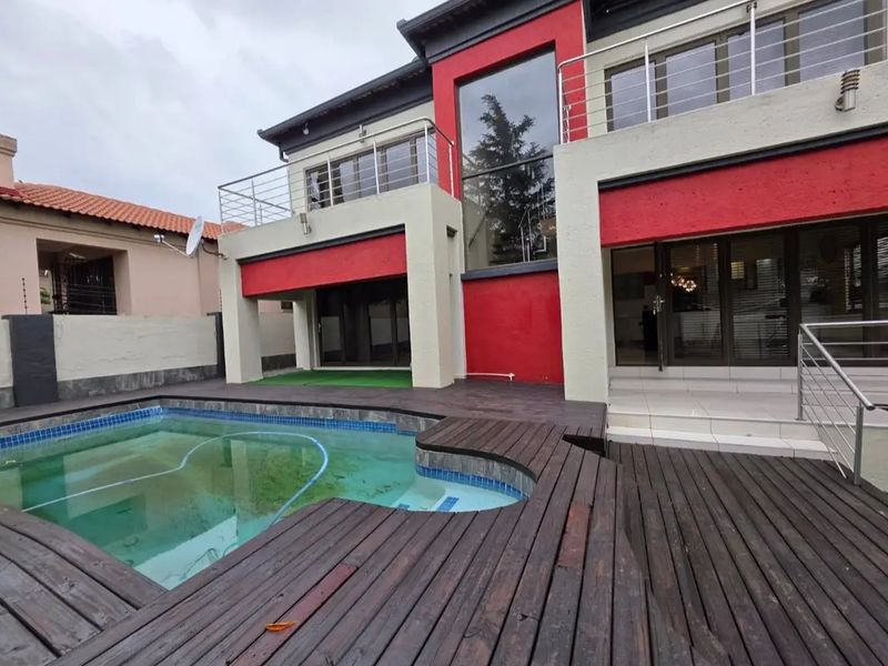 Rear exterior view featuring a swimming pool, timber decking, and a multi-level facade with a balcony and sliding glass doors.