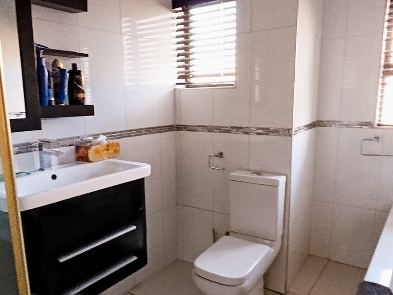 A modern bathroom featuring a vanity cabinet, basin, toilet, bathtub, and a glass-enclosed shower with tiled walls and natural light from windows.