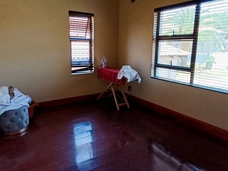 A spacious, empty bedroom featuring dark laminate flooring, neutral walls, and venetian blinds on the windows.