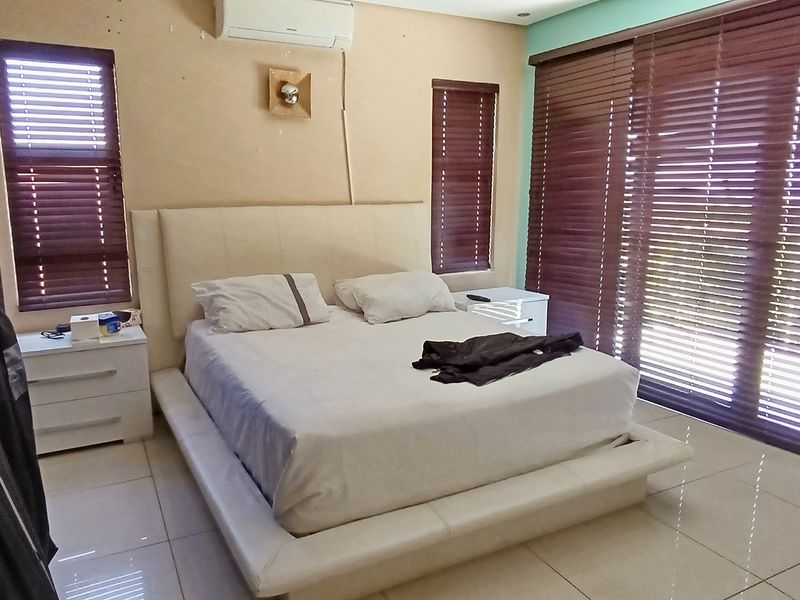 Spacious bedroom featuring tiled flooring, built-in cupboards, a split-system air conditioner, and large sliding glass doors with venetian blinds.