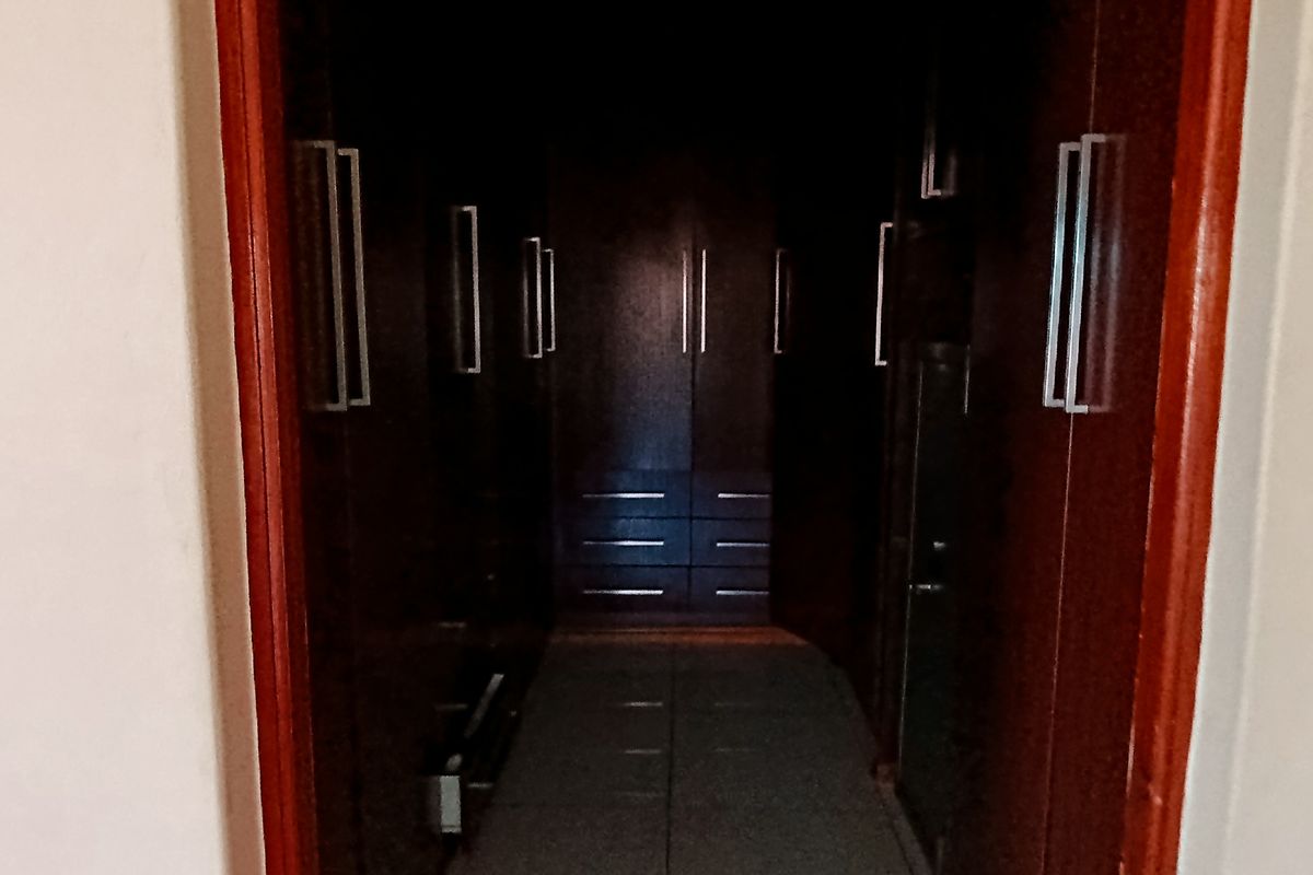 A walk-in closet area featuring dark wood built-in cupboards and tiled flooring, providing ample storage space.
