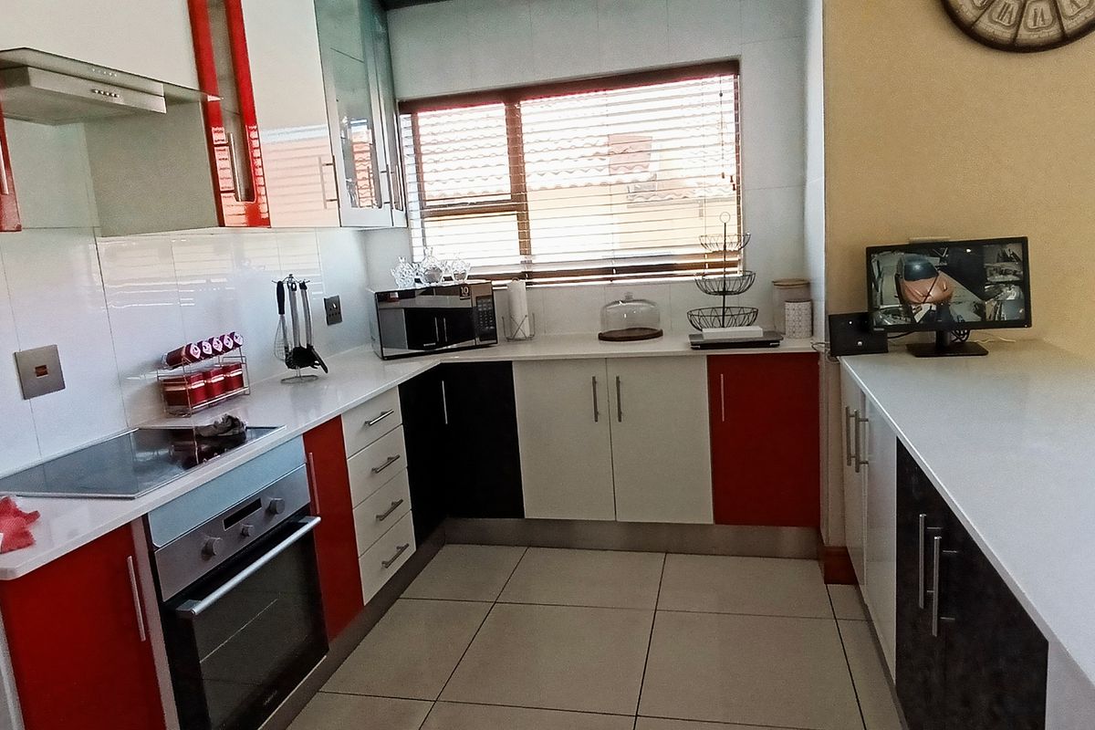 A modern kitchen featuring red and white cabinetry, stone countertops, a built-in oven, and an electric hob with a tiled backsplash.