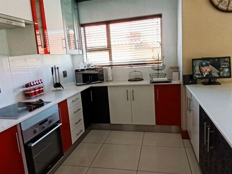 A modern kitchen featuring red and white cabinetry, stone countertops, a built-in oven, and an electric hob with a tiled backsplash.