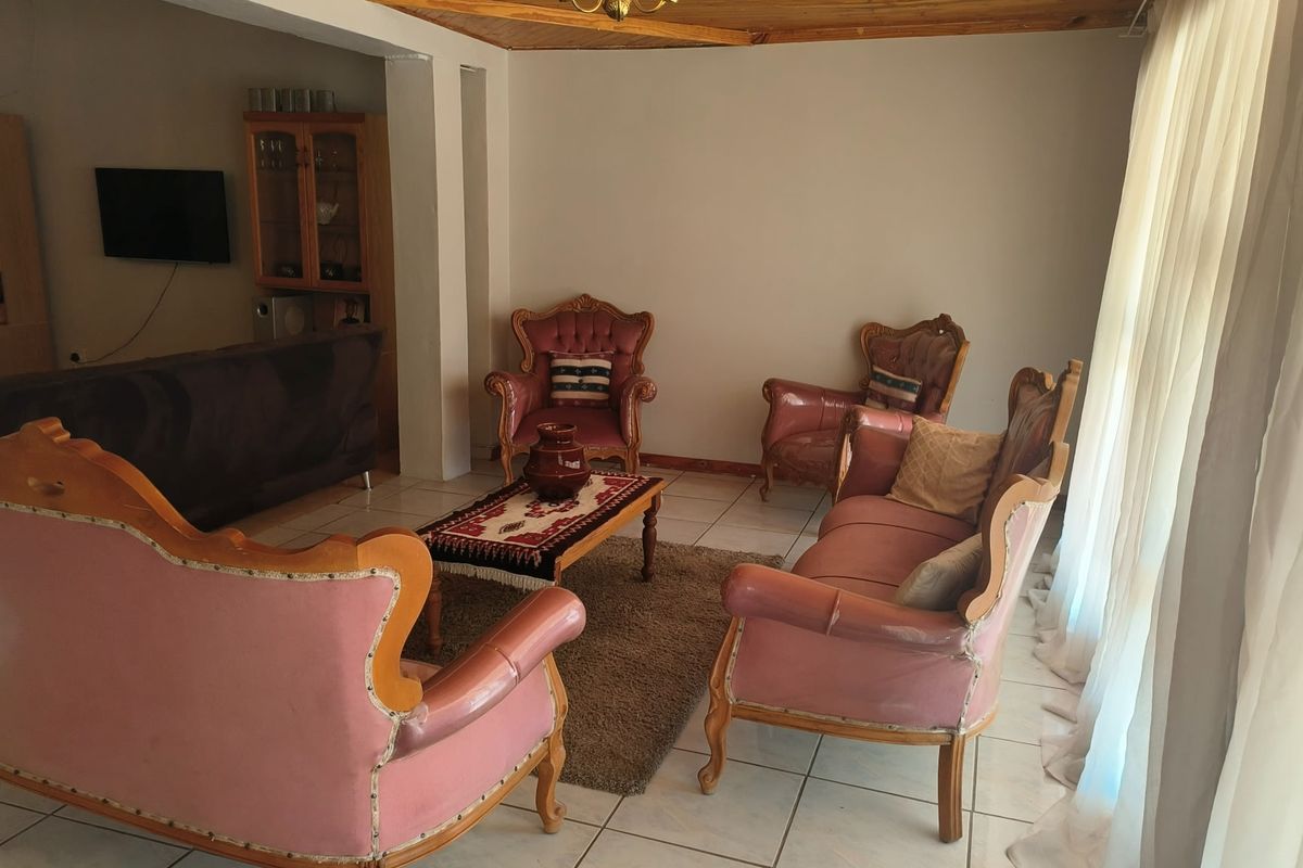 A living room featuring tiled flooring and a wooden ceiling trim, with a built-in display cabinet and natural light from large windows.