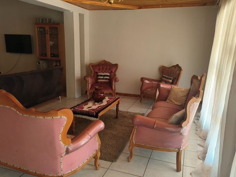 A living room featuring tiled flooring and a wooden ceiling trim, with a built-in display cabinet and natural light from large windows.