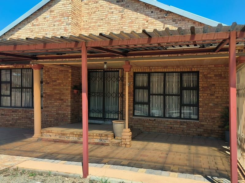 Front elevation of a face brick house featuring a covered patio area with paved flooring and secure metal entrance gates.