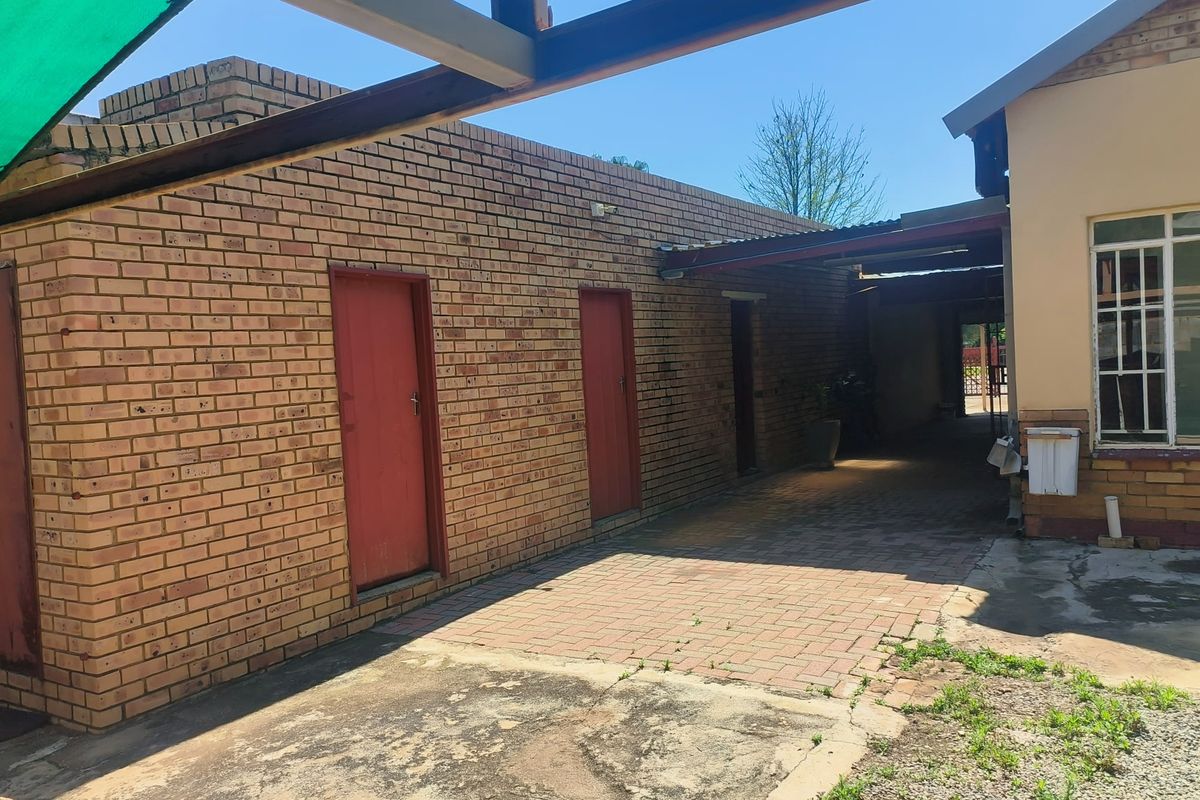 Rear exterior view showing a paved courtyard area with a covered walkway, face brick walls, and multiple access doors.