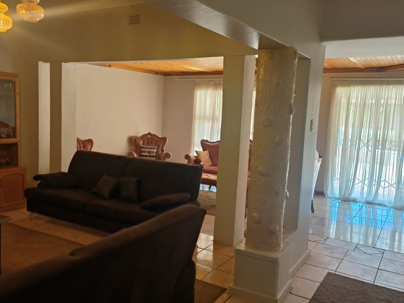 Open plan living area featuring ceramic tiled flooring, a decorative pillar, and timber ceiling accents with access to the outdoor area via sliding doors.