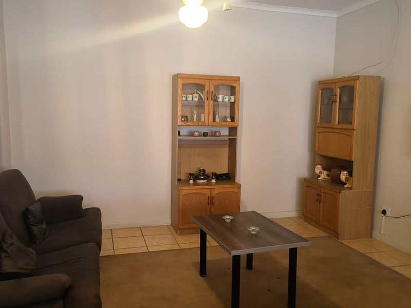 A living room featuring tiled flooring and coving, currently furnished with cabinetry and a television. The space requires minor electrical maintenance.