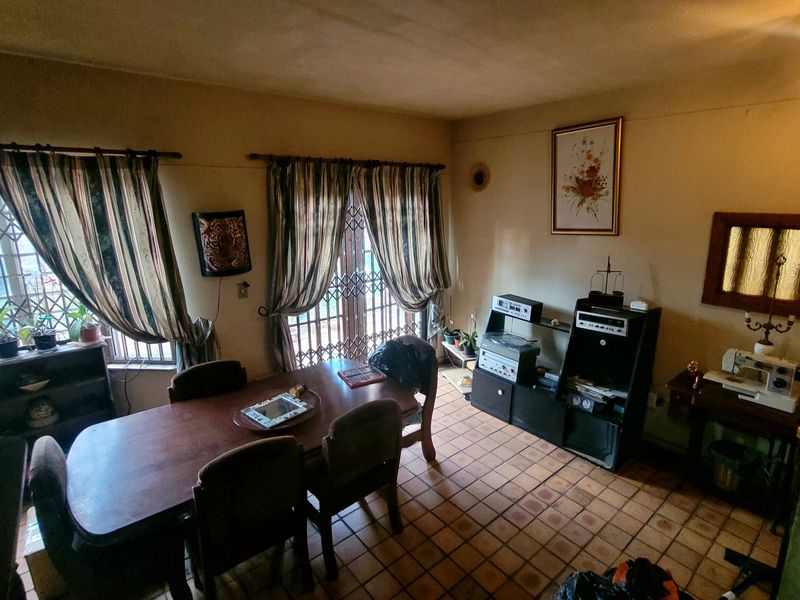 Dining room featuring terracotta floor tiles and security gates on windows and doors, offering a dated interior space ready for modernization.