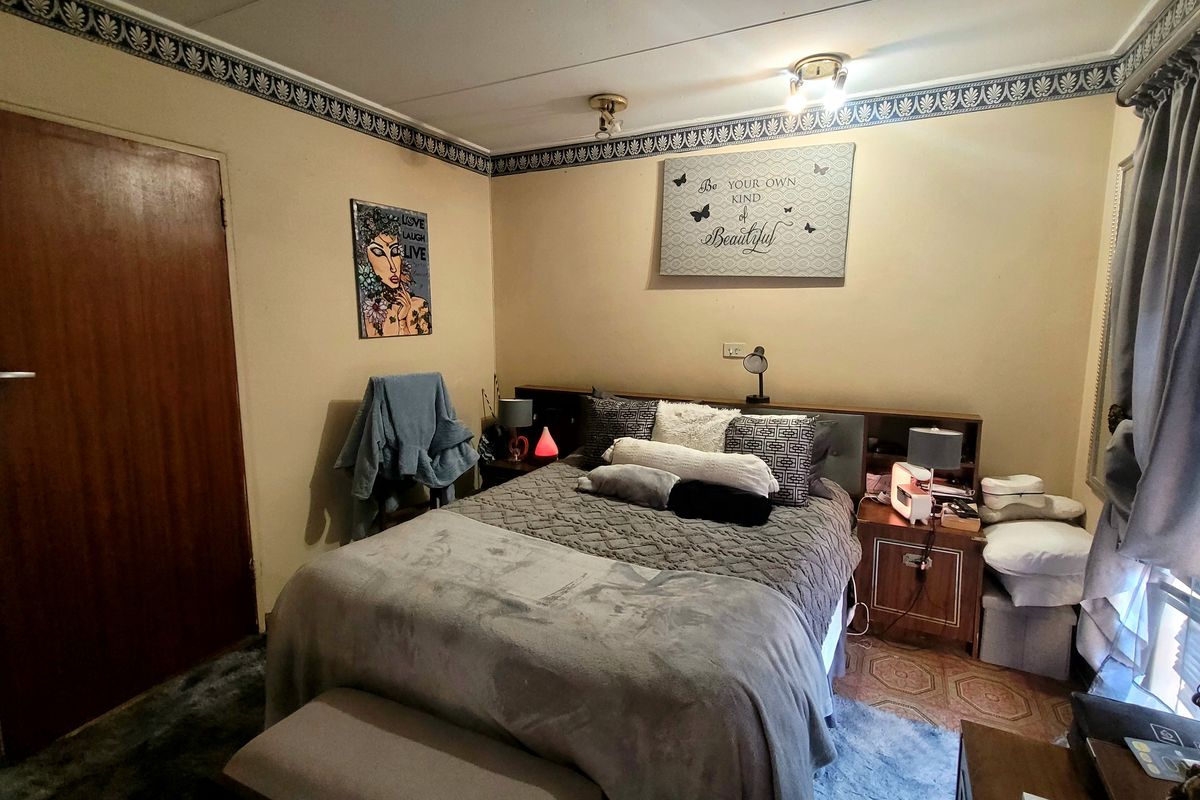 A functional bedroom featuring a built-in headboard, decorative wallpaper border, and ceiling-mounted lighting, offering a dated but well-maintained living space.