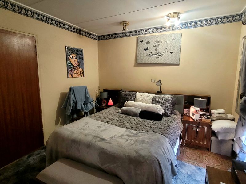 A functional bedroom featuring a built-in headboard, decorative wallpaper border, and ceiling-mounted lighting, offering a dated but well-maintained living space.
