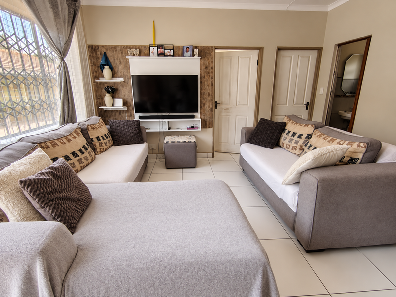 A well-maintained living room featuring tiled flooring, a built-in media unit, and direct access to adjacent rooms.