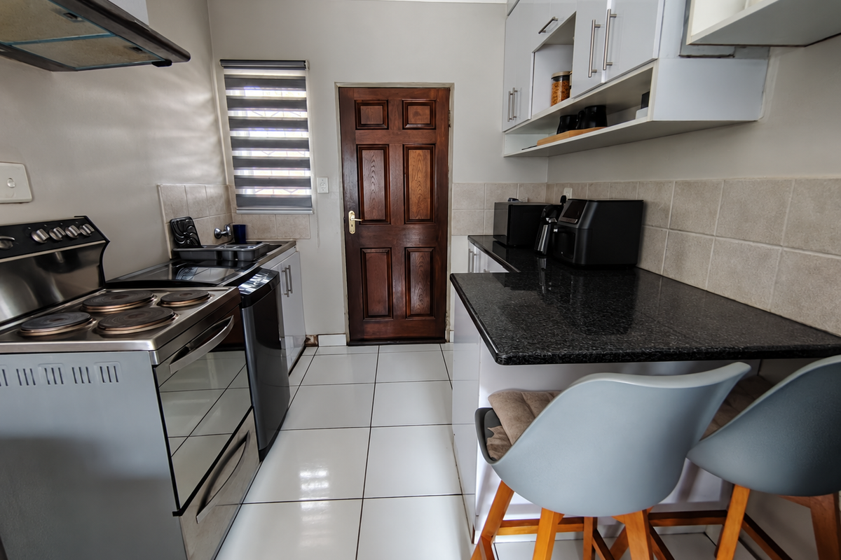 A functional kitchen featuring granite countertops, white cabinetry, tiled flooring, and a built-in electric stove with an overhead extractor fan.