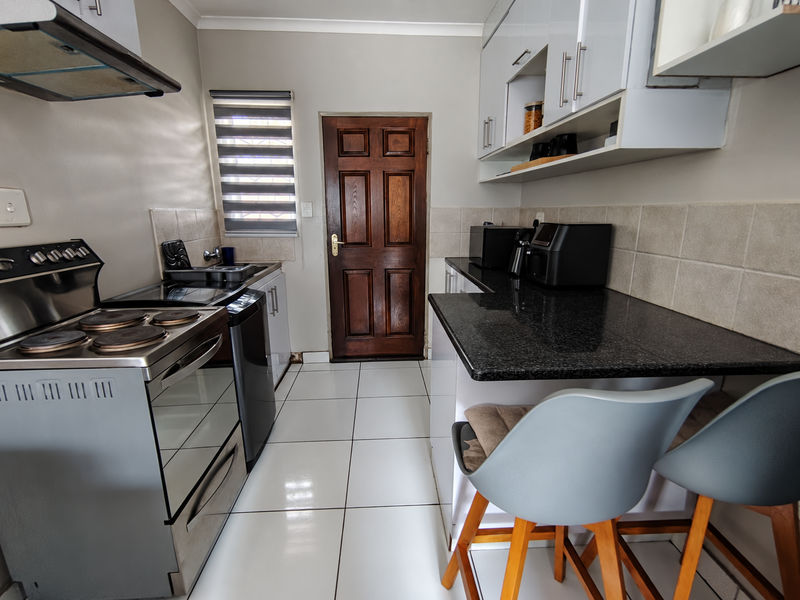 A functional kitchen featuring granite countertops, white cabinetry, tiled flooring, and a built-in electric stove with an overhead extractor fan.
