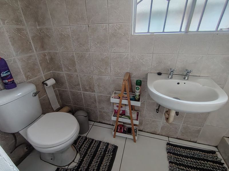 A compact bathroom featuring a wall-mounted basin, close-coupled toilet, and neutral ceramic tiling throughout.