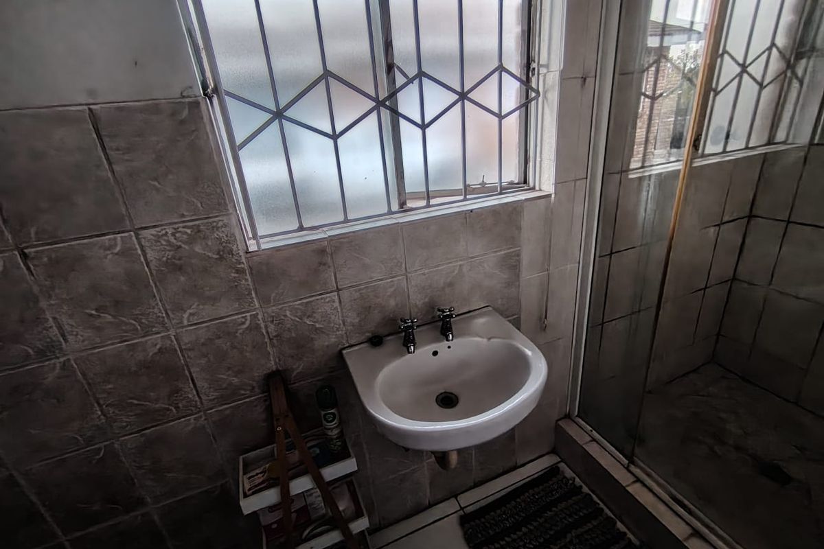 A functional bathroom featuring a wall-mounted basin, tiled finishes, and a shower enclosure, requiring cosmetic updates to improve its overall condition.