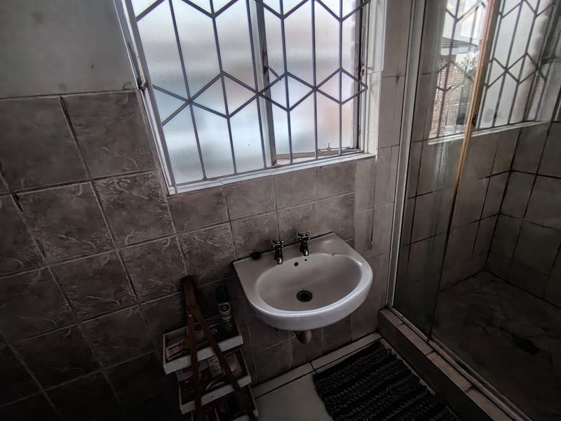 A functional bathroom featuring a wall-mounted basin, tiled finishes, and a shower enclosure, requiring cosmetic updates to improve its overall condition.