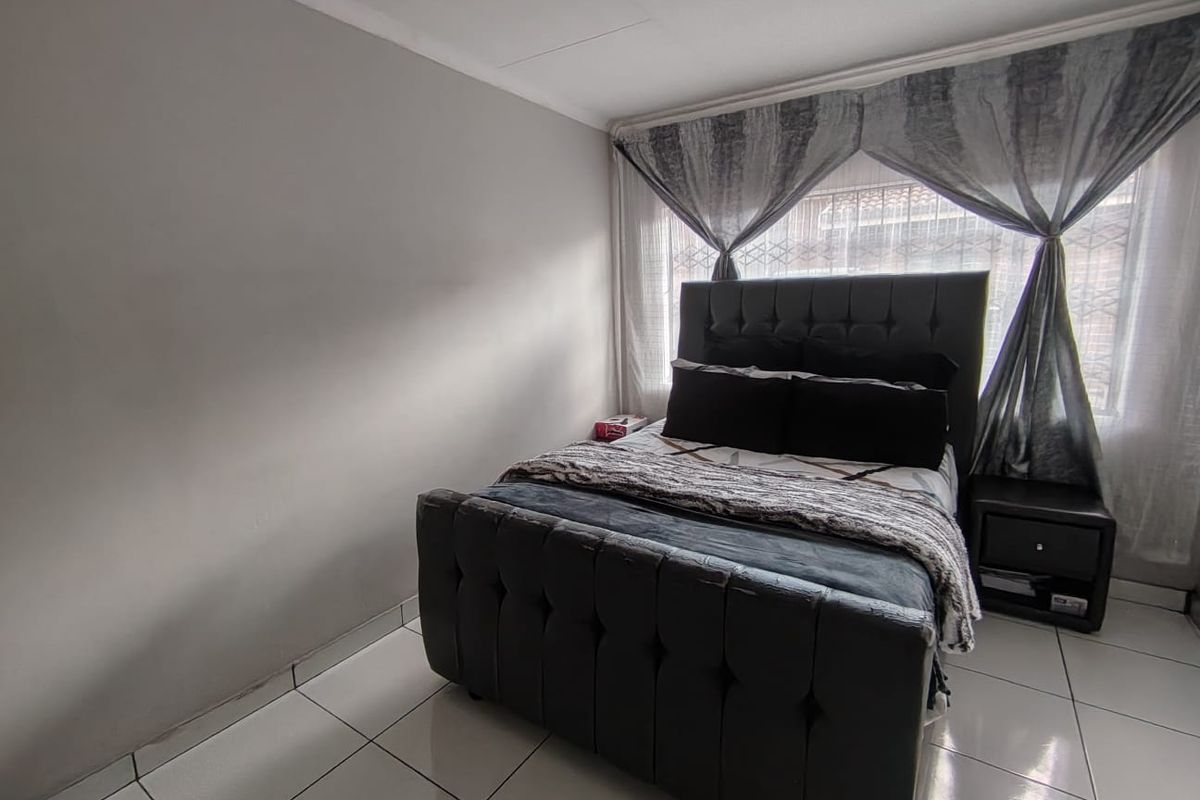 A bedroom featuring tiled flooring and a window fitted with security bars, providing a functional and secure living space.