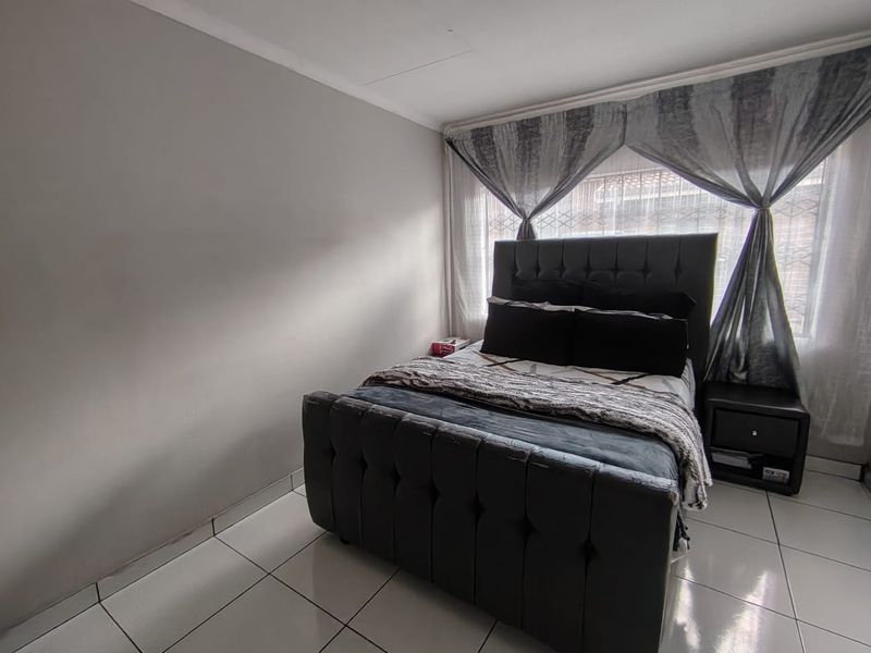 A bedroom featuring tiled flooring and a window fitted with security bars, providing a functional and secure living space.