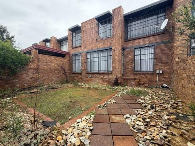Rear view of a double-story face brick townhouse featuring a private garden with a paved walkway and security bars on windows.