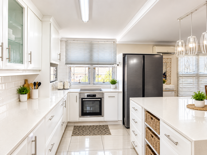 Modern, well-lit kitchen featuring white cabinetry, quartz countertops, subway tile backsplash, and high-quality built-in appliances with a central island.