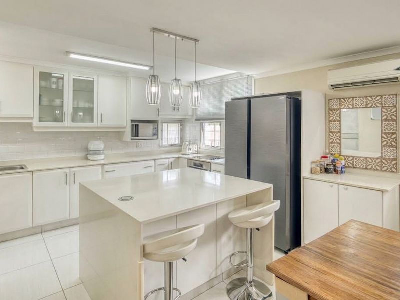 Modern kitchen featuring white cabinetry, stone countertops, a central island, subway tile backsplash, and integrated appliances, offering a clean and functional culinary space.