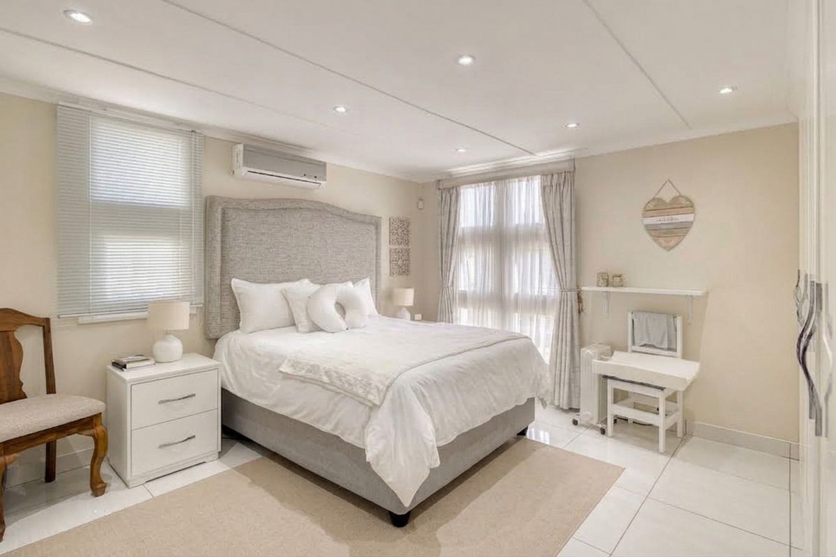 A well-maintained bedroom featuring tiled flooring, recessed downlighting, and a split-system air conditioning unit, offering a bright and comfortable living space.