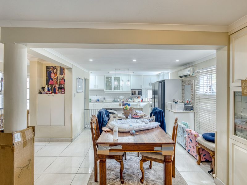 Open-plan living and dining area featuring tiled flooring, recessed lighting, and a functional kitchen with built-in cabinetry and integrated appliances.