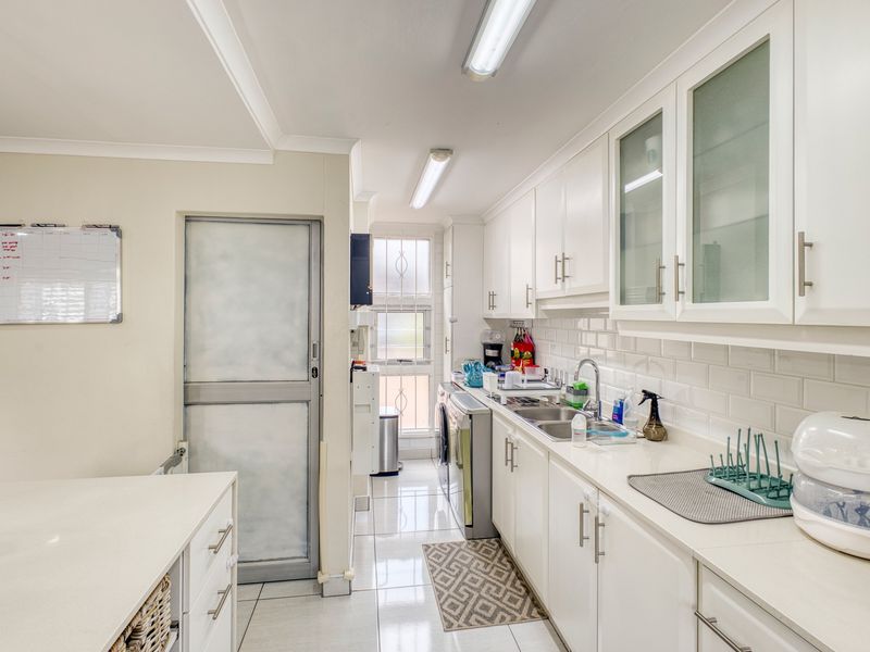 A functional scullery featuring white cabinetry, subway tile backsplash, stainless steel sink, and tiled flooring, providing additional prep and wash-up space.